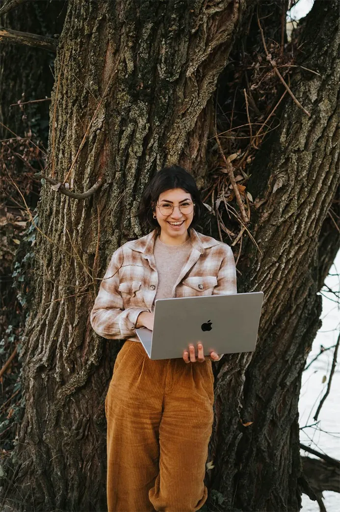 Portrait de Chloé, graphiste éco-responsable, riante, en nature, avec son ordinateur en main.